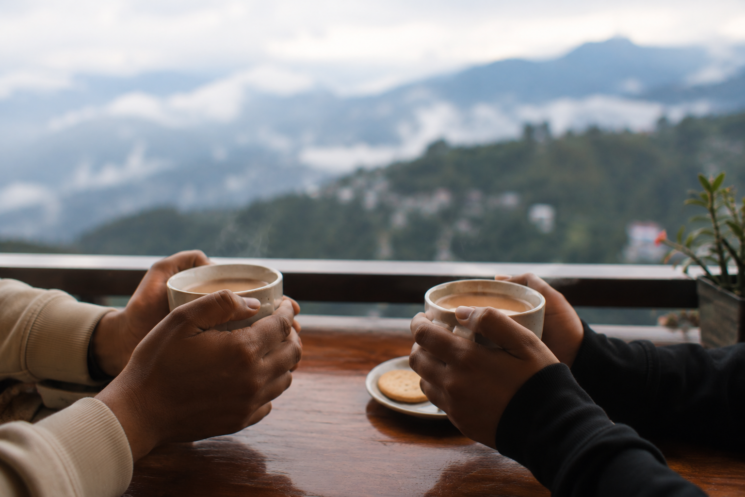 Two hands holding warm cups of Darjeeling tea with a misty mountain view