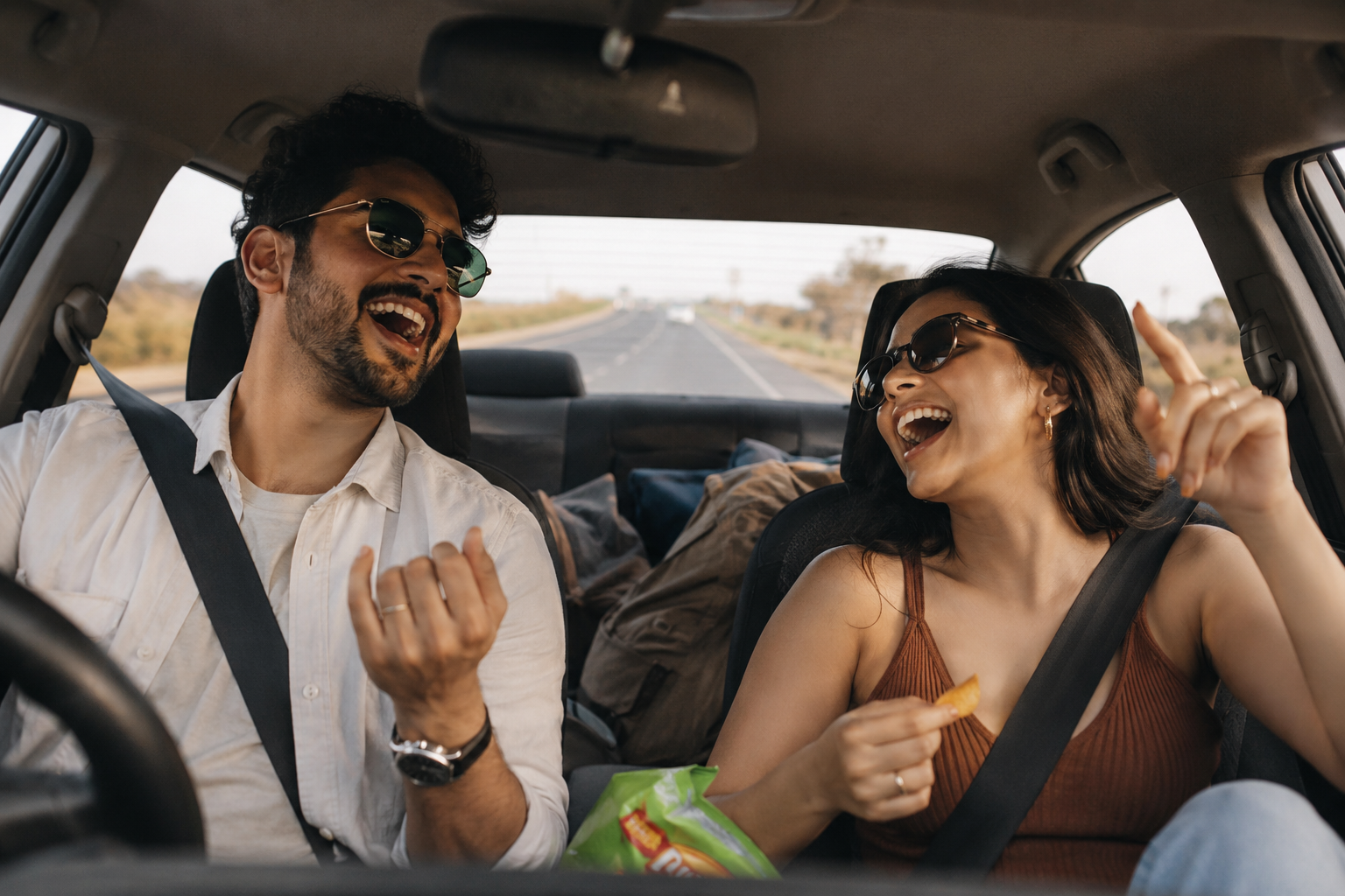 A couple laughing and singing along to music inside a car on an open road
