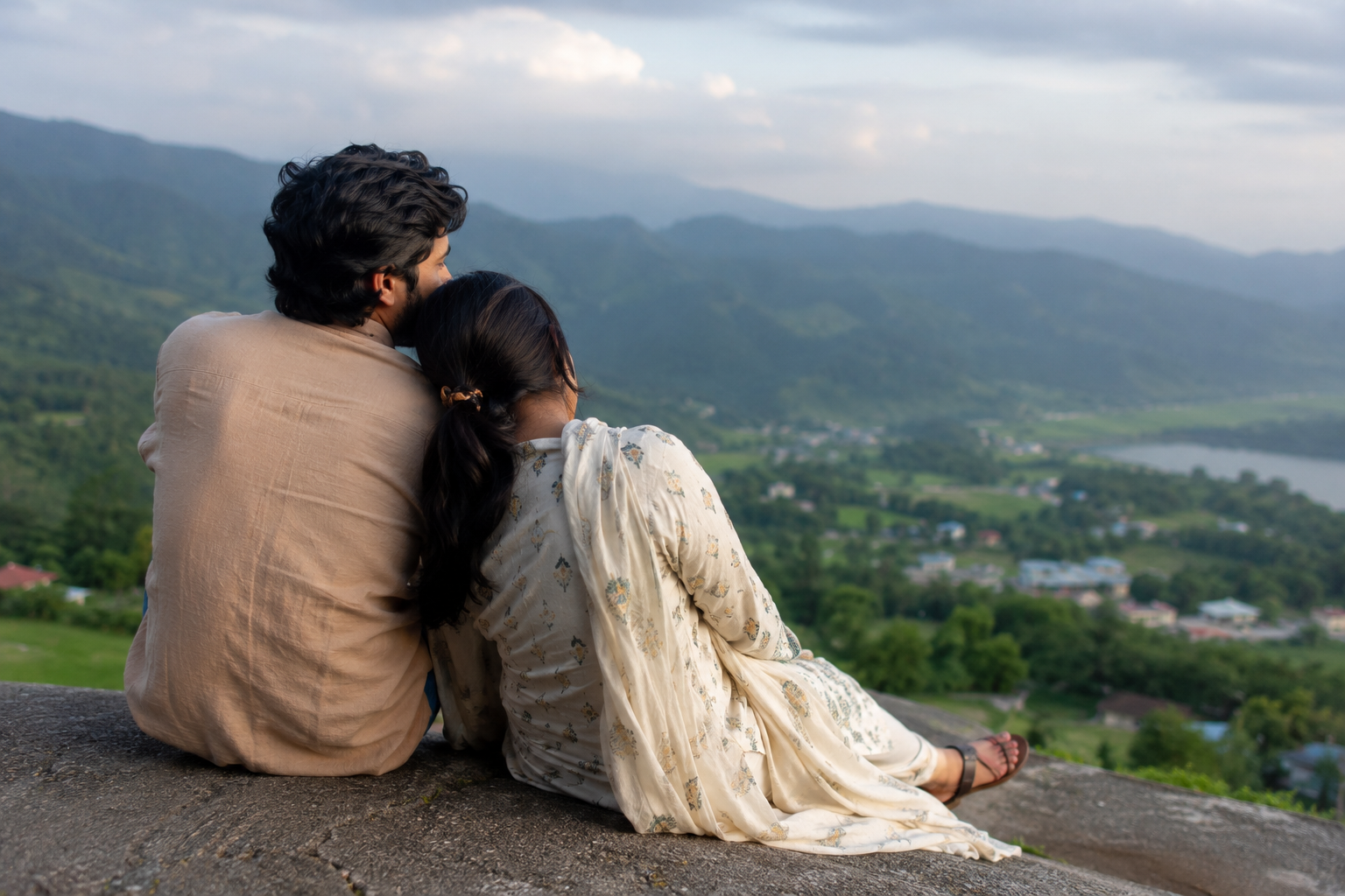 A couple sitting together on a quiet ledge overlooking a green valley